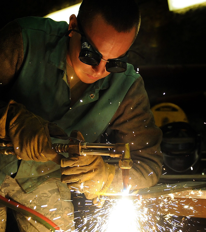 A man welding in the dark with safety goggles on.