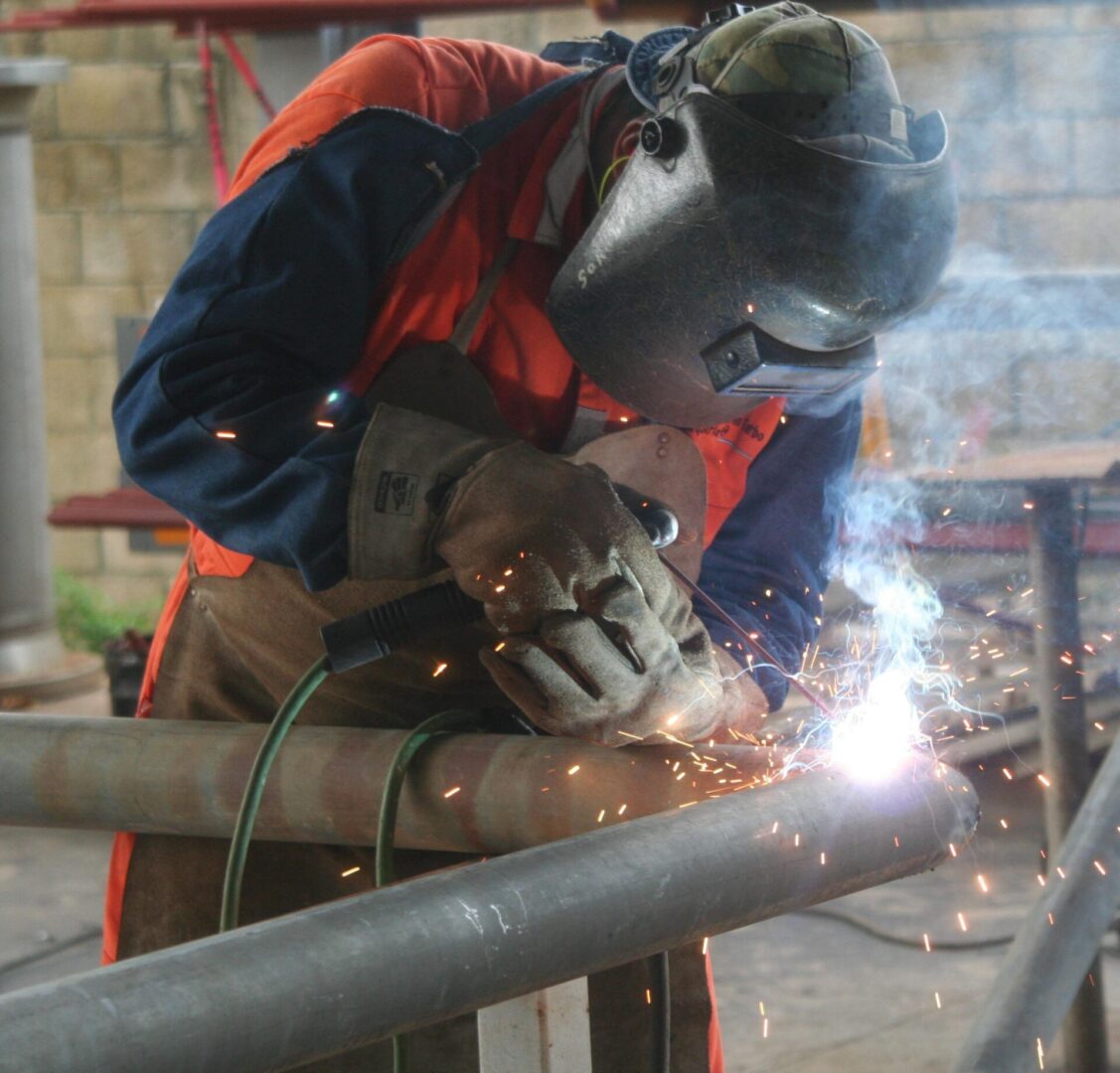 A man welding metal pipe with an electric welder.